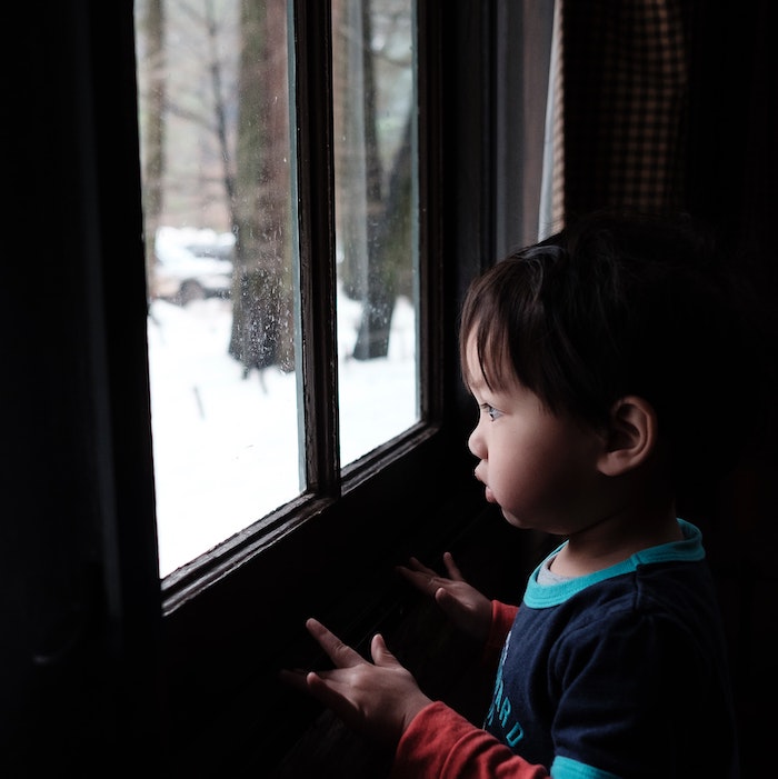 Little boy staring out the window at snow outside