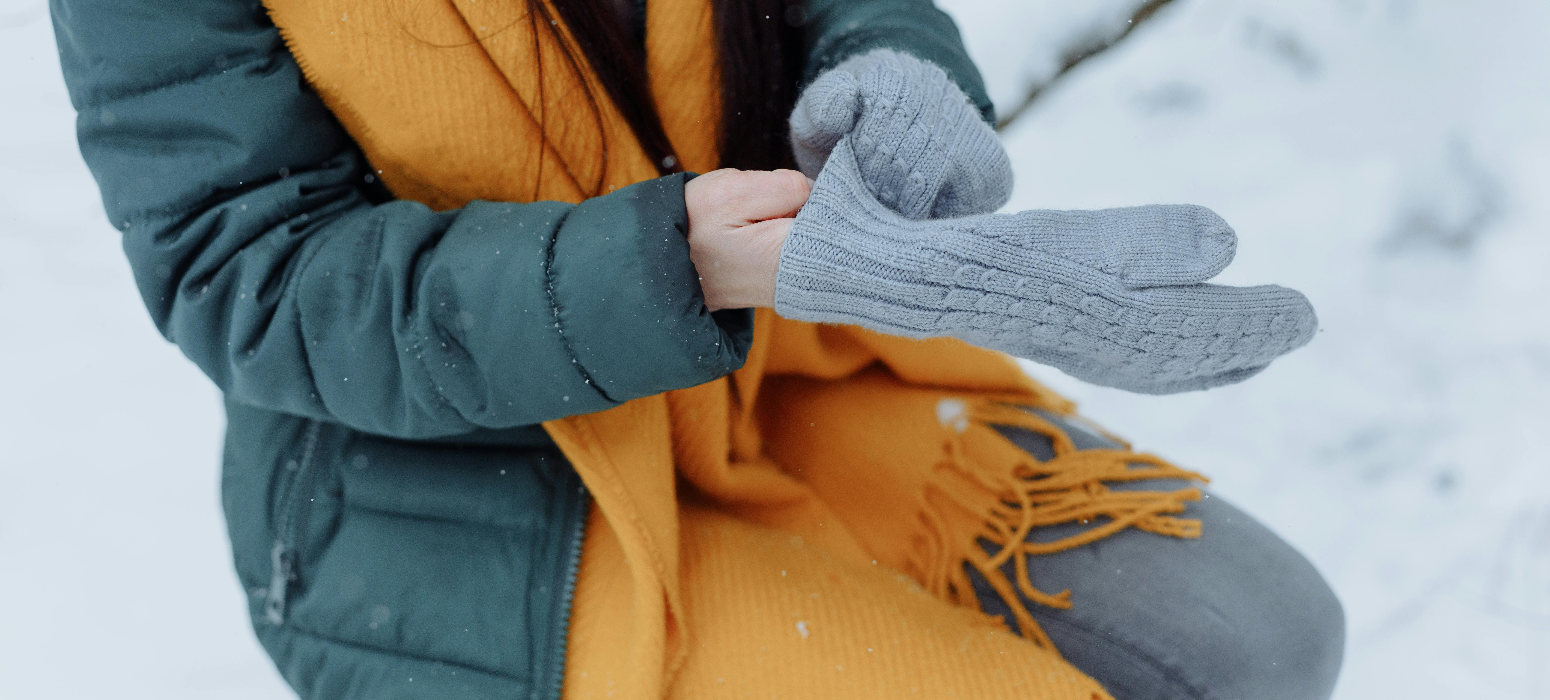 A woman placing her cold hands in her mitten out in the snow.