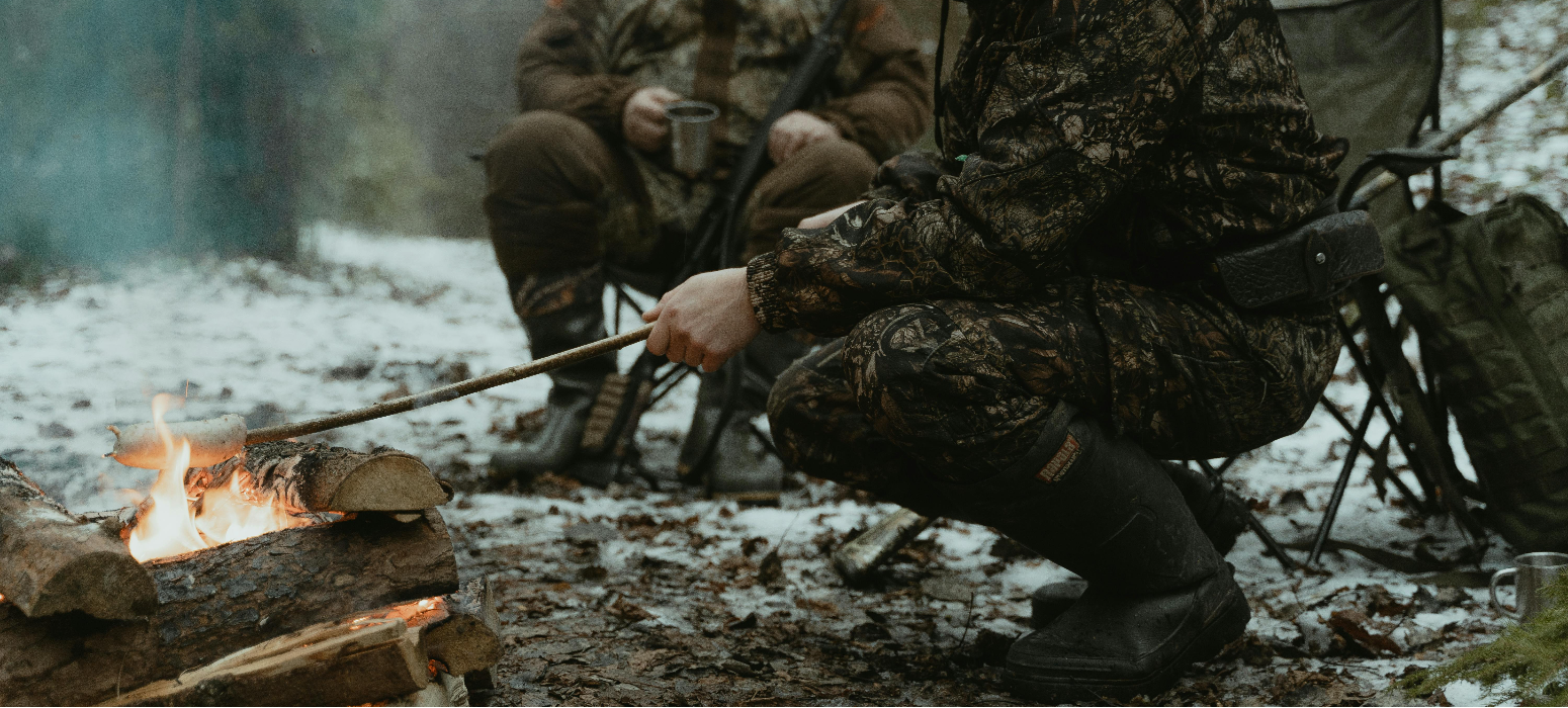 Two men sitting by a fire while hunting in the cold.