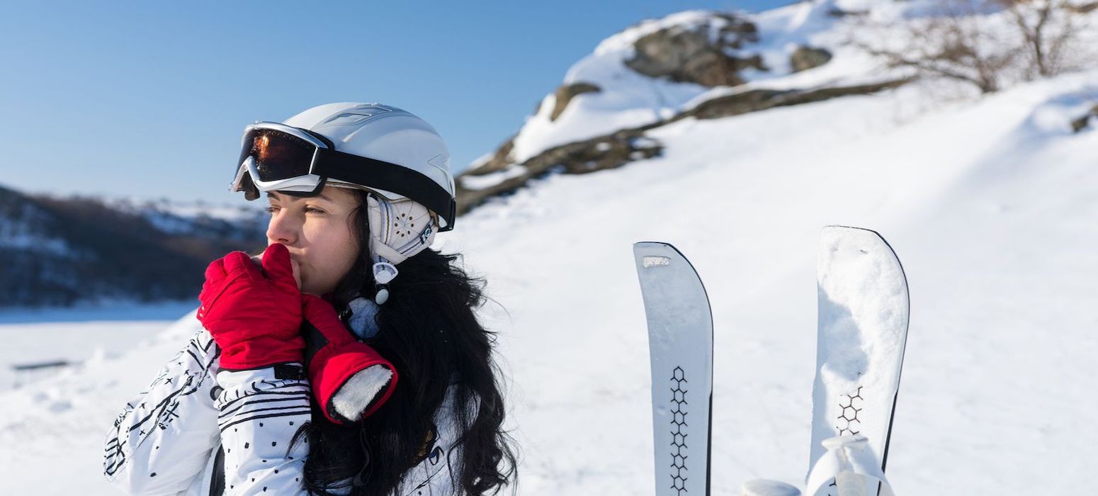 A skier on top of a mountain keeping her hands warm in the cold weather.